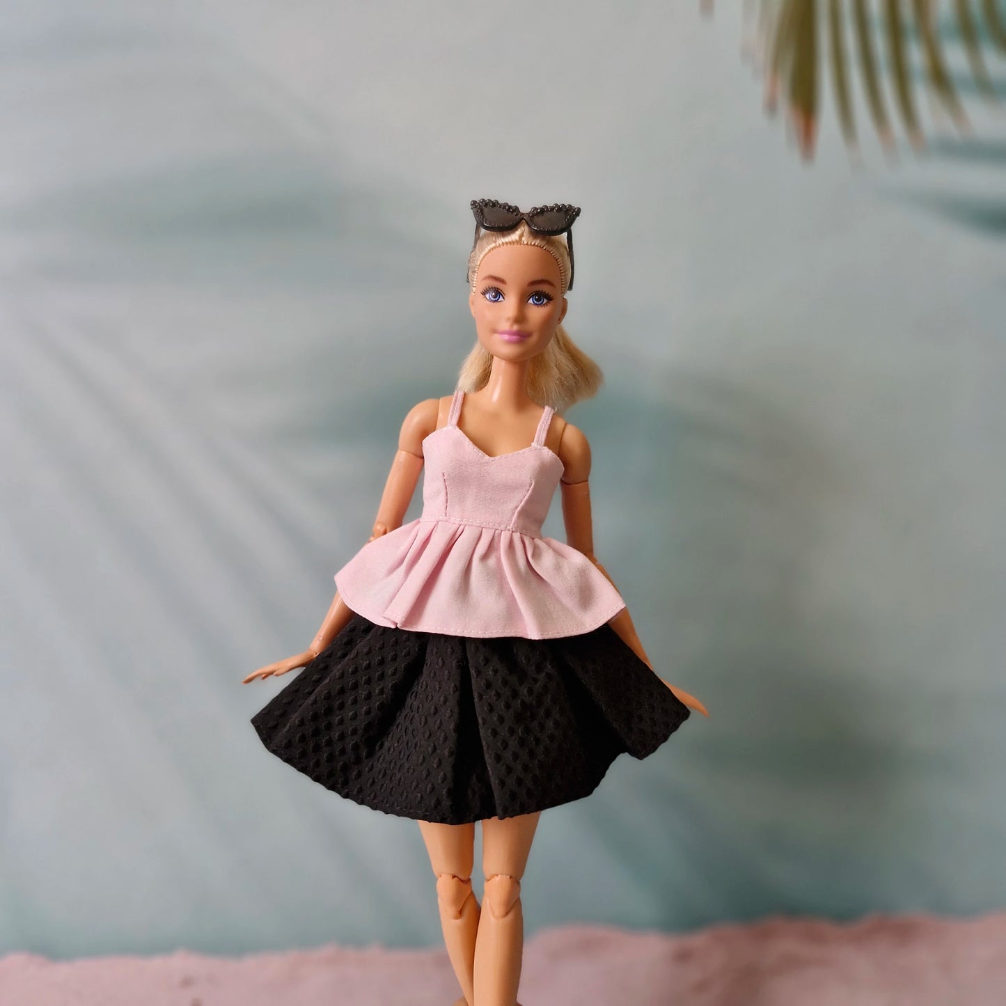 Barbie doll wearing a pink top and black skirt with a blurred background