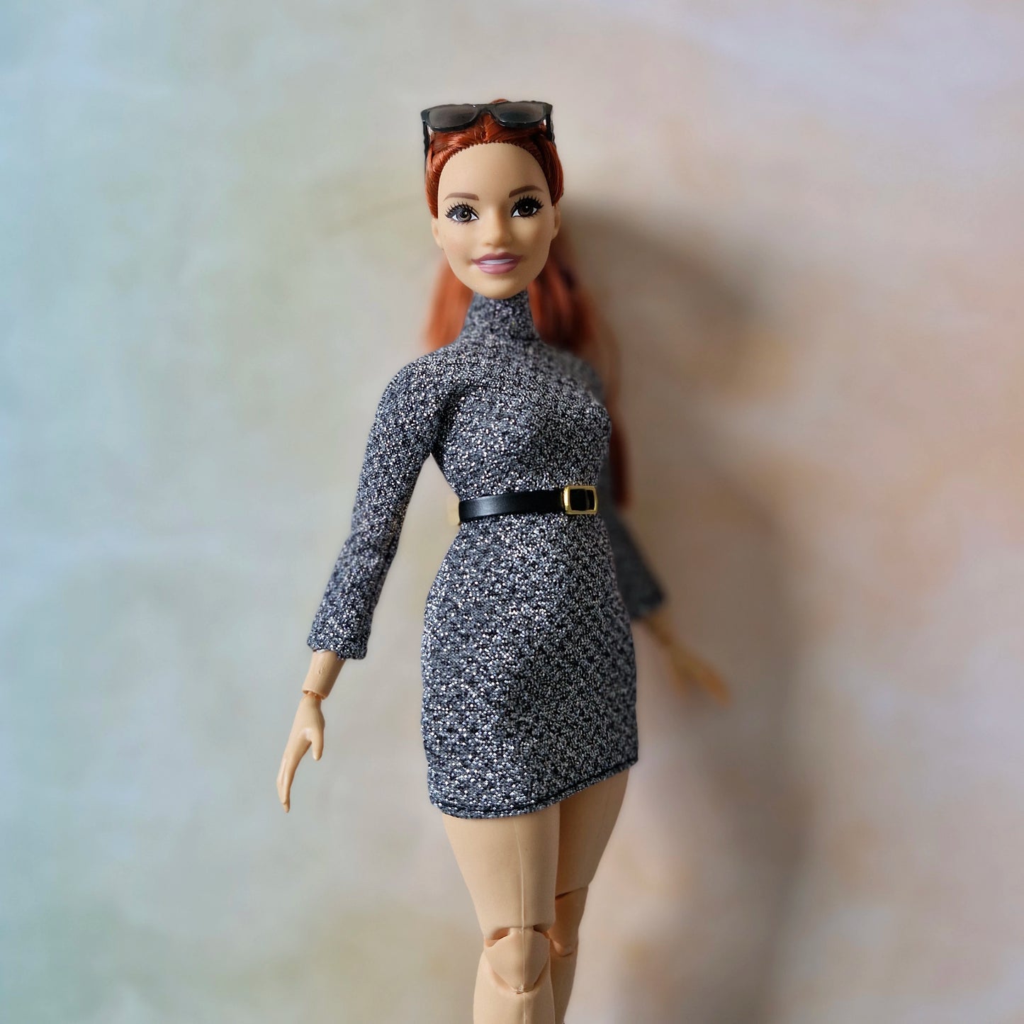 Barbie doll wearing a patterned dress with a belt and knee-high boots on a neutral background