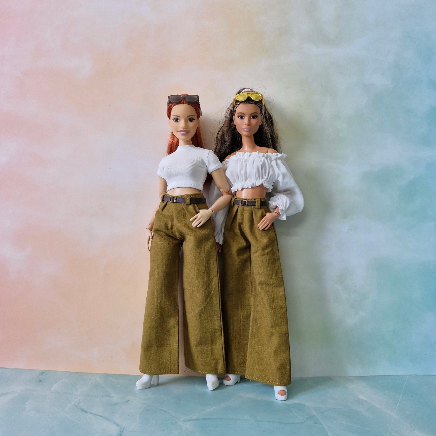 Two dolls wearing matching outfits with wide-leg pants against a pastel gradient background