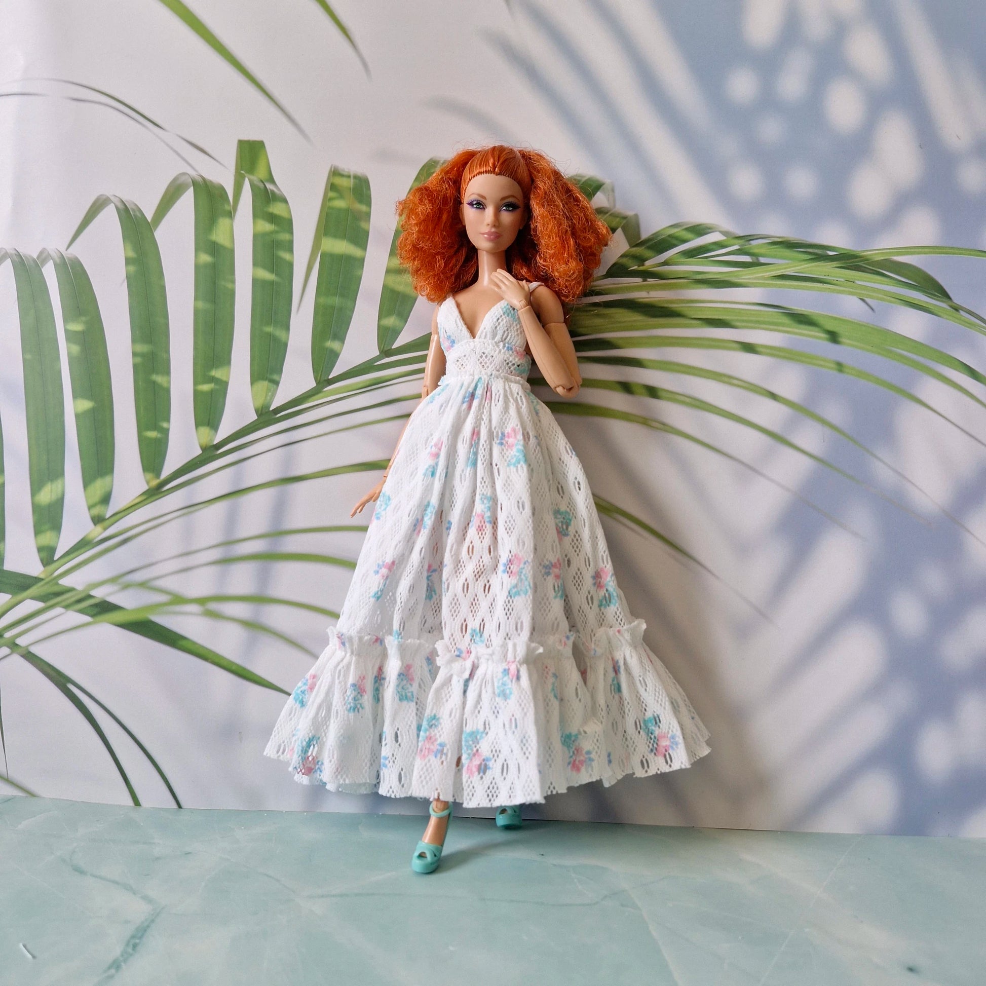 Doll in a floral dress standing against a leafy background