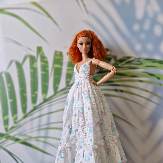 Barbie doll in a white floral dress standing against a leafy background