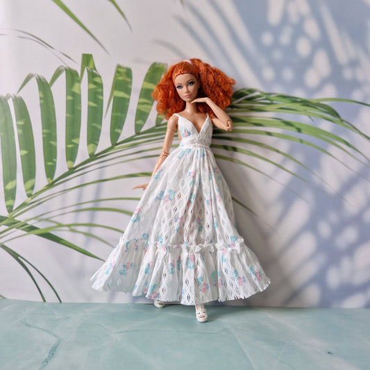 Doll in a white floral dress standing against a leafy green background