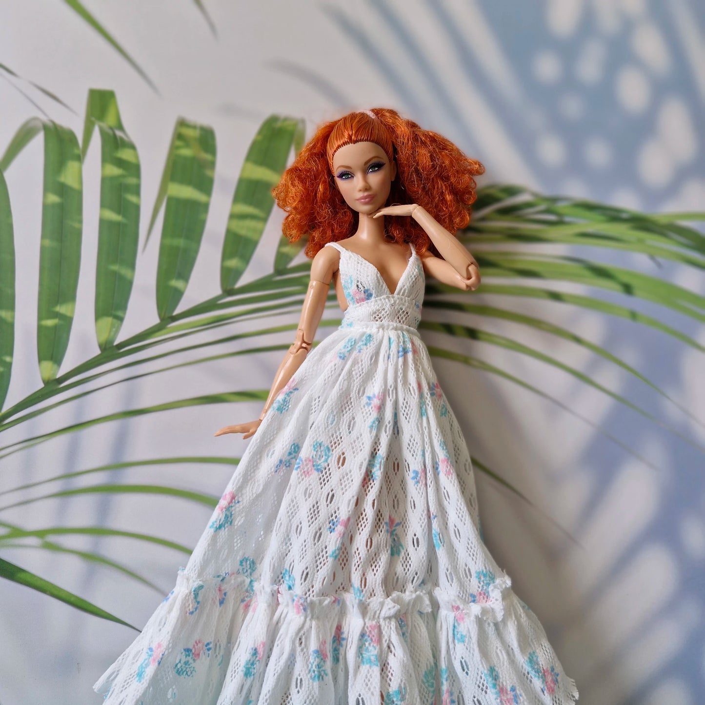 Barbie doll in a white floral dress standing against a leafy background