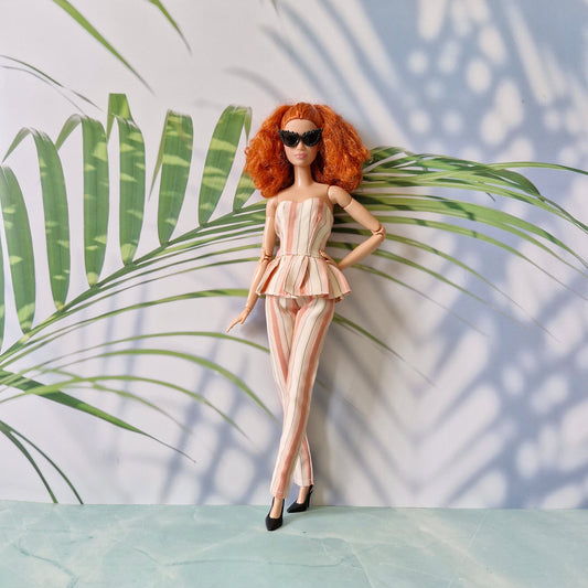 Barbie doll in a striped outfit with sunglasses standing against a leafy background