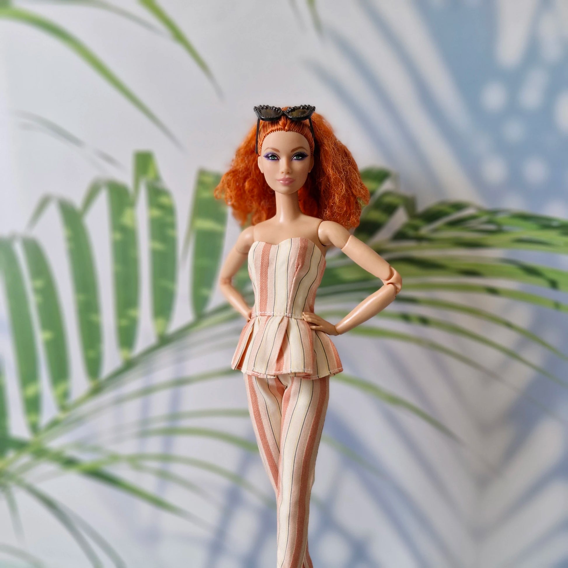 Barbie doll with red hair and a striped outfit standing against a leafy background