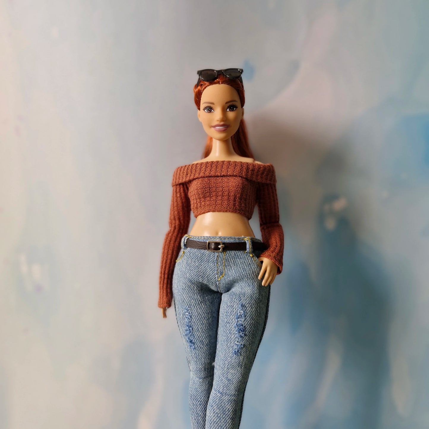 Barbie doll wearing a brown sweater and blue jeans against a neutral background