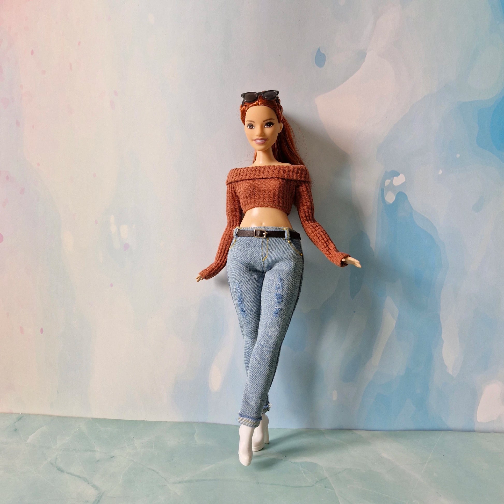 Barbie doll wearing a brown top and blue jeans against a textured wall.