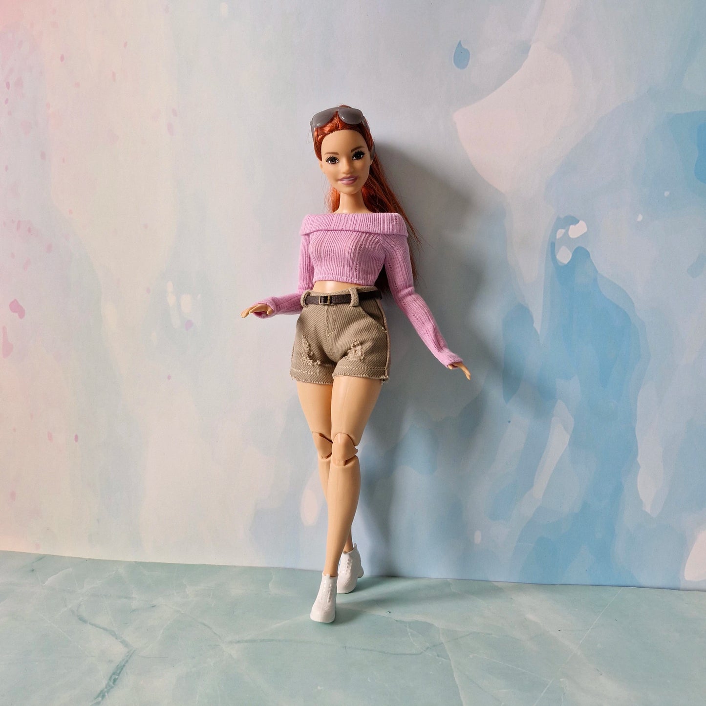 Barbie doll wearing a pink top and beige shorts against a pastel background