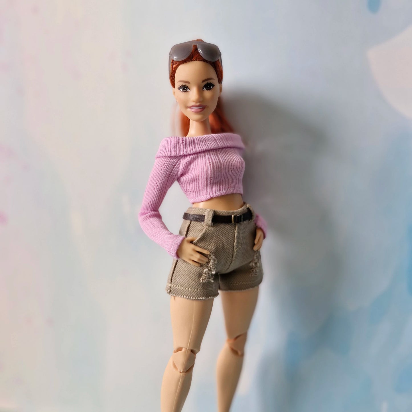 Barbie doll wearing a pink sweater and beige shorts against a plain background