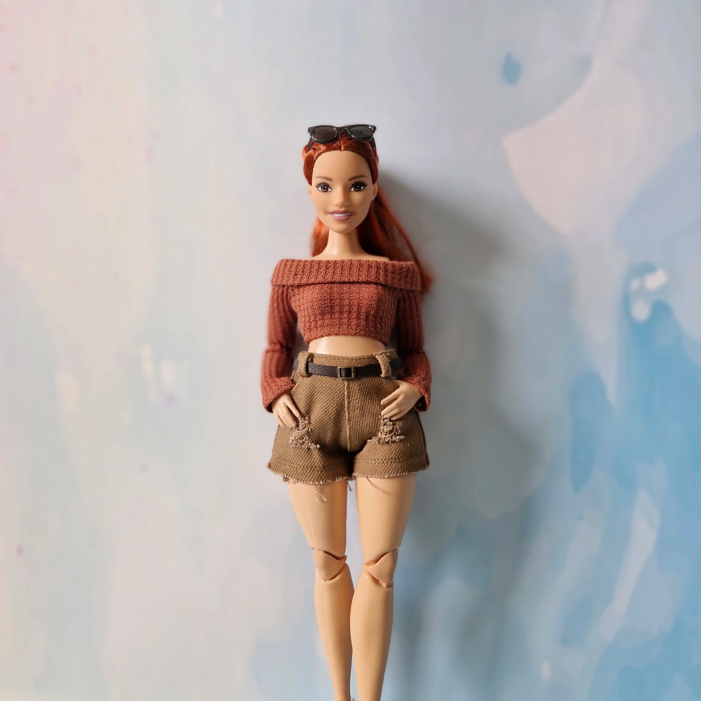 Barbie doll wearing a brown sweater and shorts against a light background