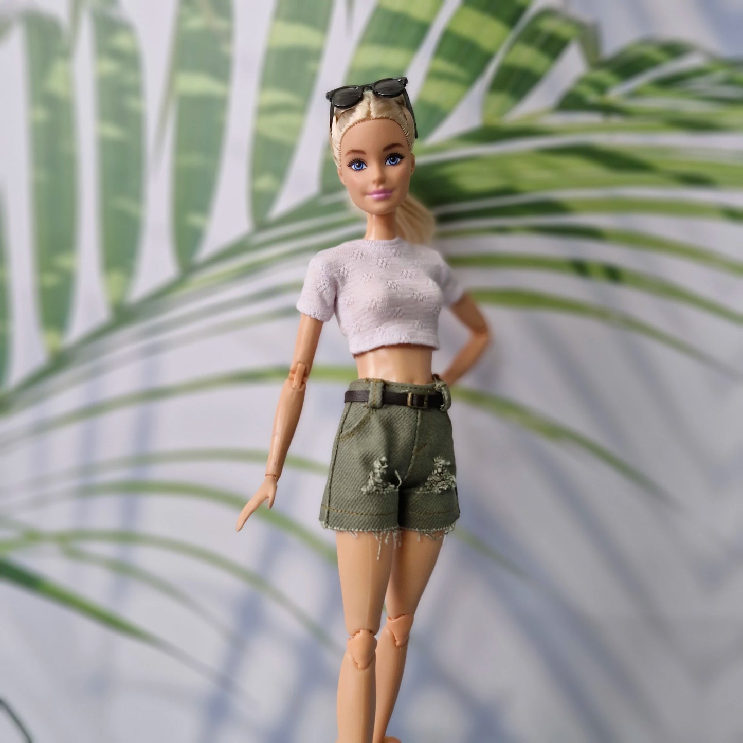 Barbie doll wearing a white top and green shorts with a palm leaf background