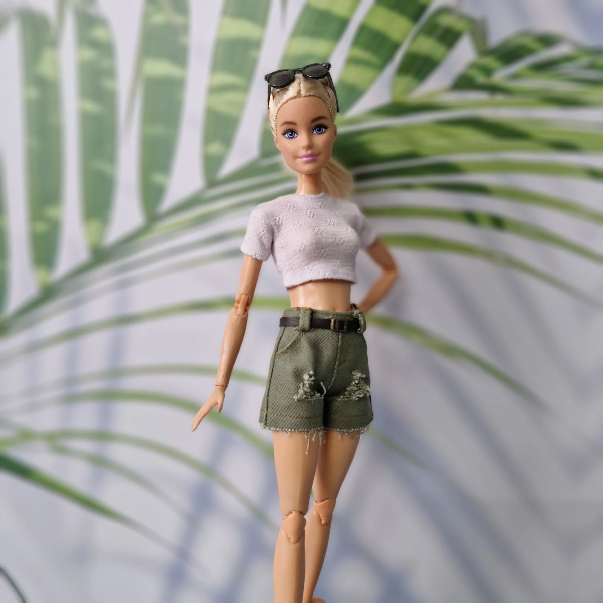 Barbie doll wearing a white top and green shorts with a palm leaf background
