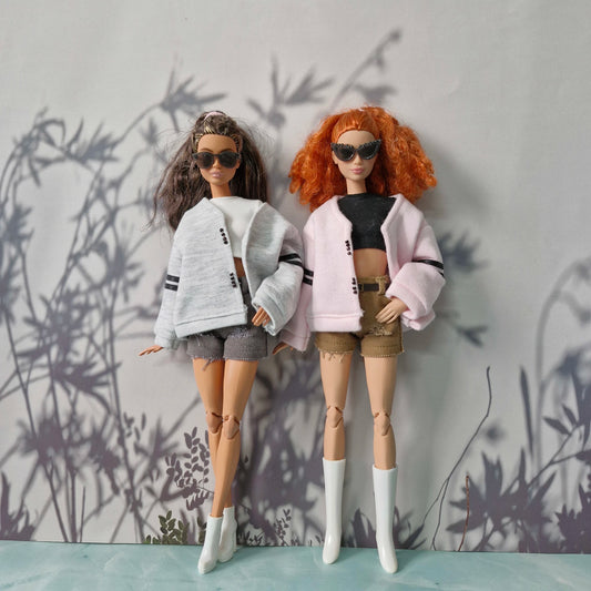 Two Barbie dolls in layered outfits with cardigans and belted shorts