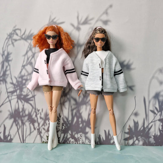 Two dolls wearing matching outfits with cardigans against a gray wall with plant shadows.