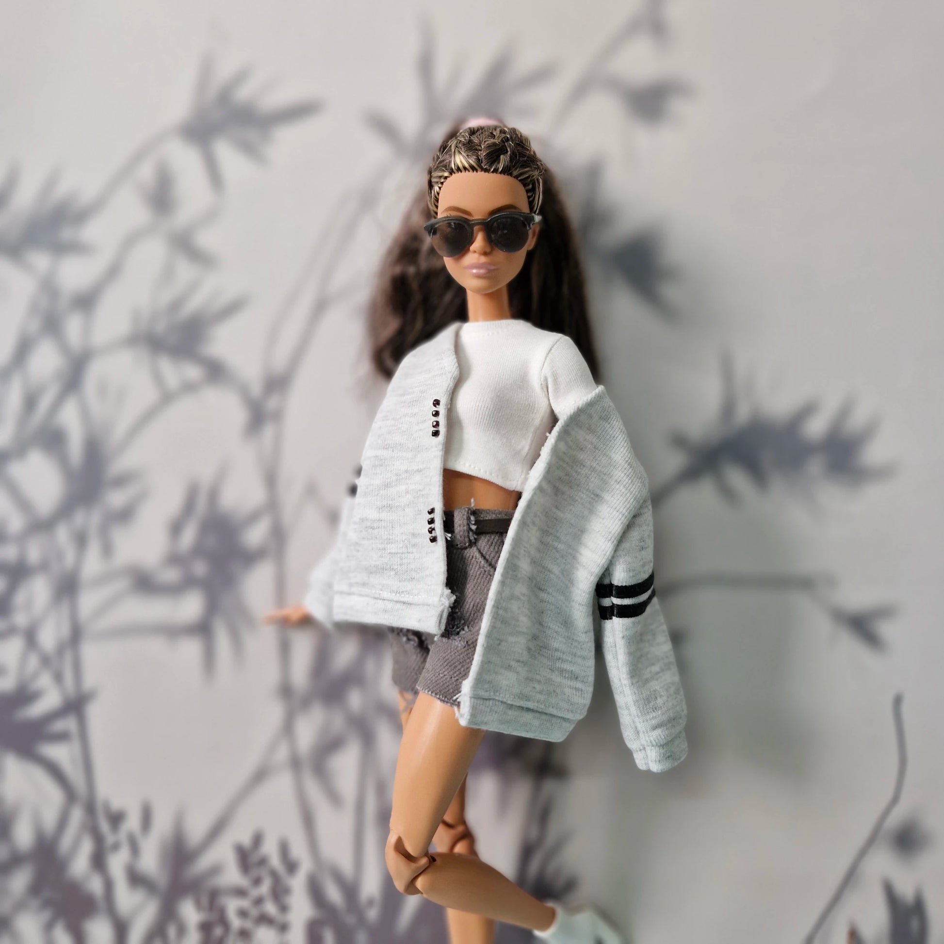 Barbie doll wearing a white top, gray cardigan, and sunglasses against a neutral background
