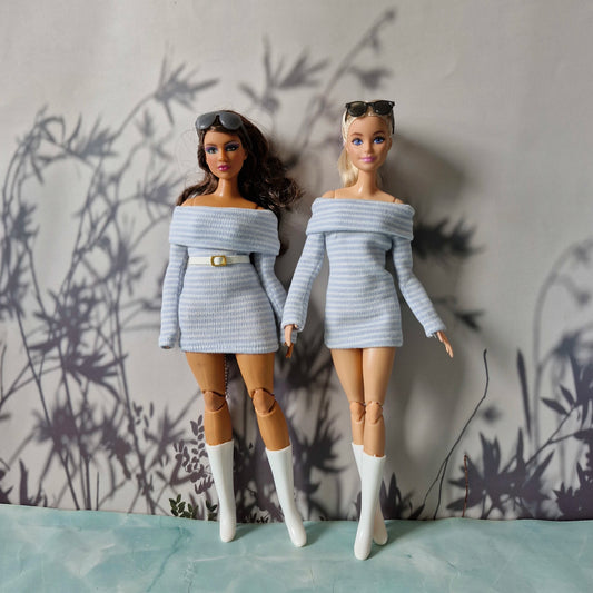Two dolls wearing matching off-shoulder sweaters against a textured wall.