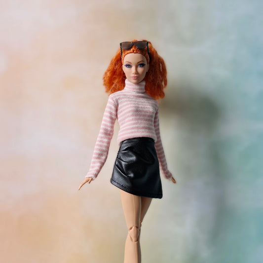 Barbie doll in pink striped turtleneck sweater and black faux-leather mini skirt standing against pastel background.