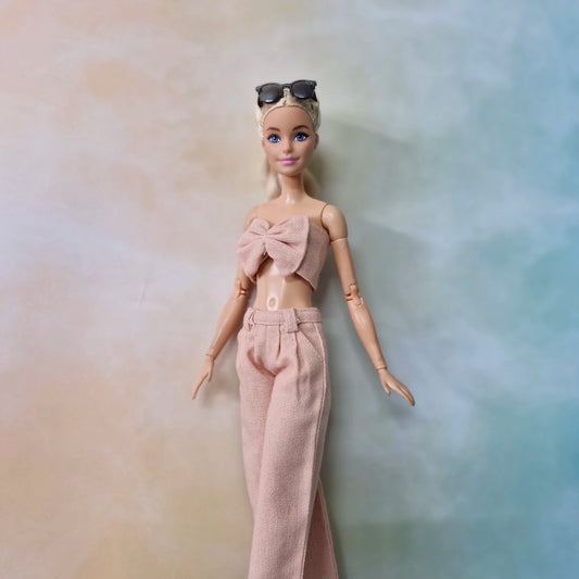 Barbie wearing blush pink bow top and matching wide-leg pants in a soft pastel background.