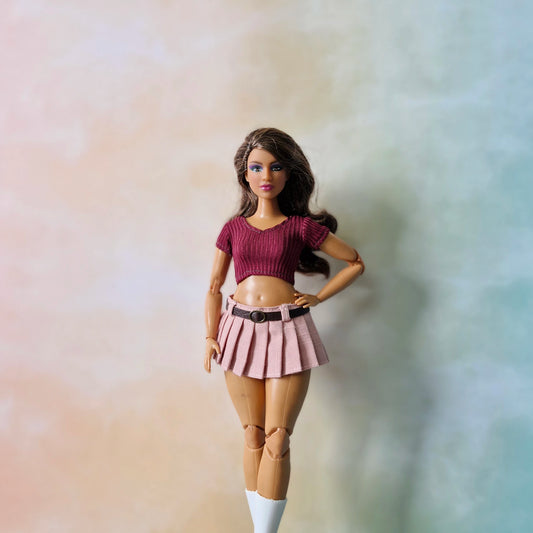 Barbie doll wearing a maroon top and pink pleated skirt against a gradient background