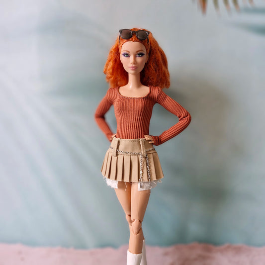 Curvy fashion doll posing in orange ribbed shirt and khaki mini skirt with silver chain