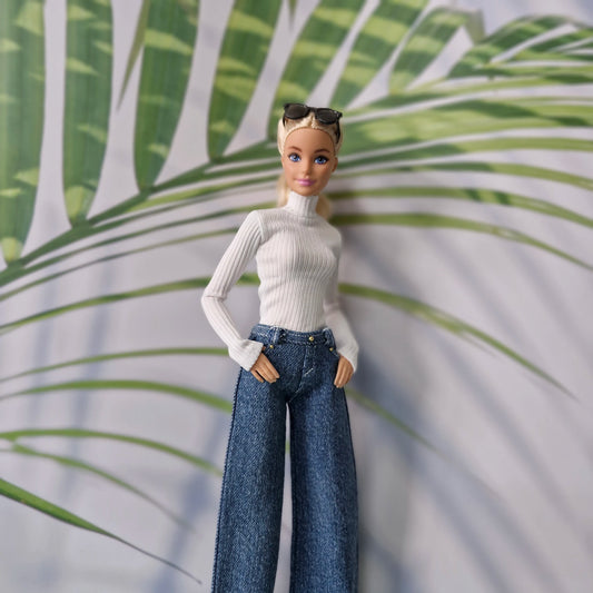 Close up of Barbie doll modeling a white long sleeve top and dark denim wide leg pants