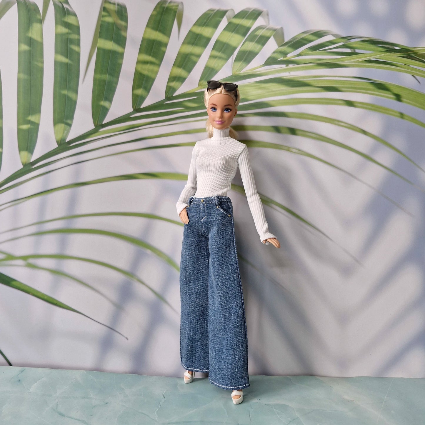 Barbie doll wearing a white top and blue jeans against a leafy green background