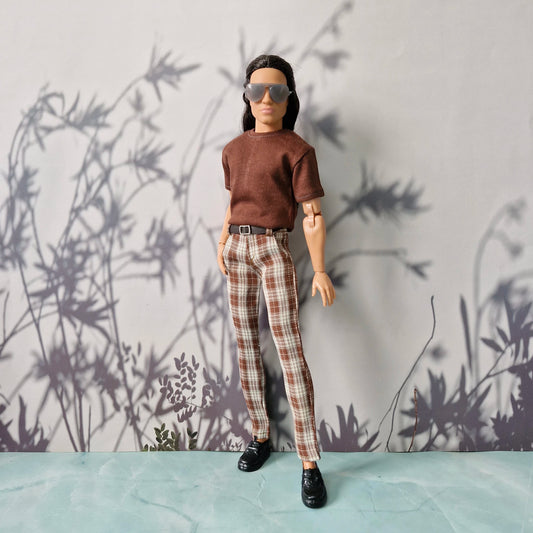 Ken Doll wearing a brown shirt and plaid pants against a wall with plant shadows