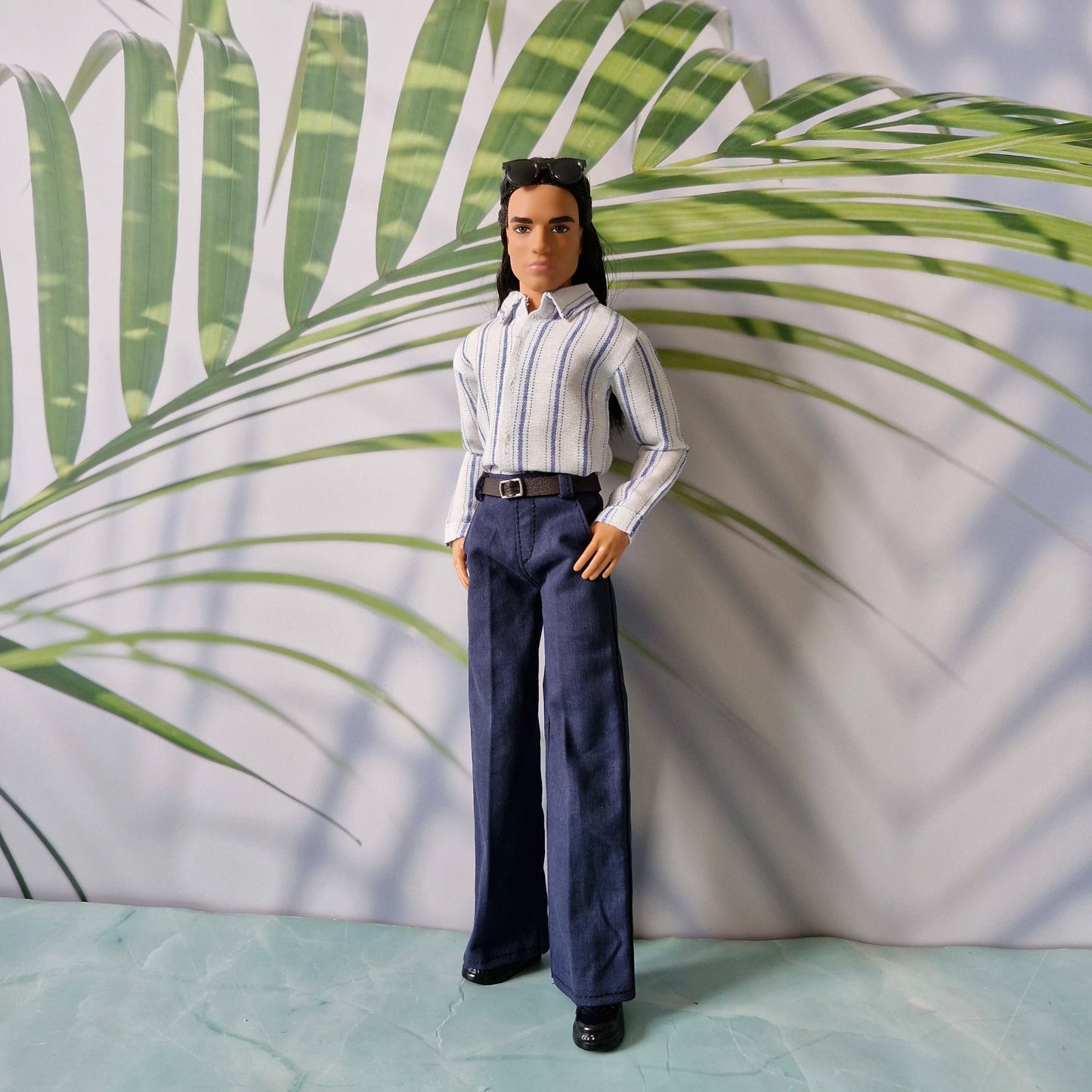 Full length shot of a Ken doll showcasing a classic menswear outfit with a striped shirt and navy blue belted pants.