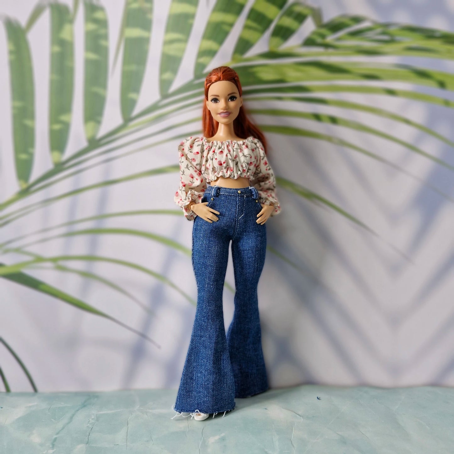 Redhead doll with hands in pockets wearing a pink floral blouse and dark wash flared jeans for Curvy Barbie.