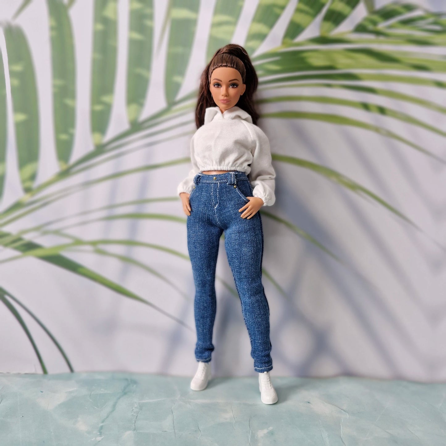 Brunette fashion doll with hands in pockets wearing a white hoodie and dark wash skinny jeans for Curvy Barbie.