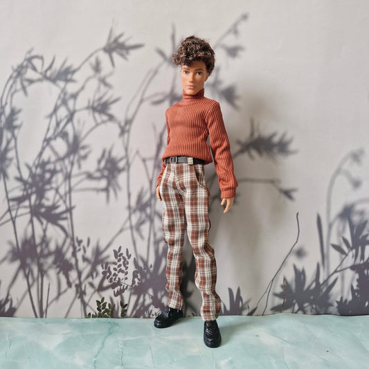 Full body shot of a male fashion doll wearing a brown sweater and plaid trousers for Ken.