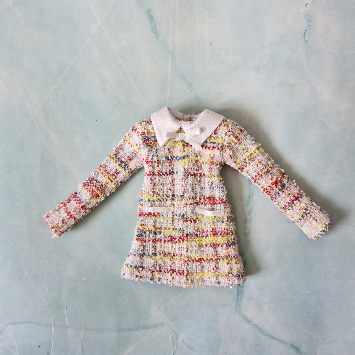 Flat lay of a handmade 1/6 scale multi-color tweed dress with a white collar and white bow for Barbie.