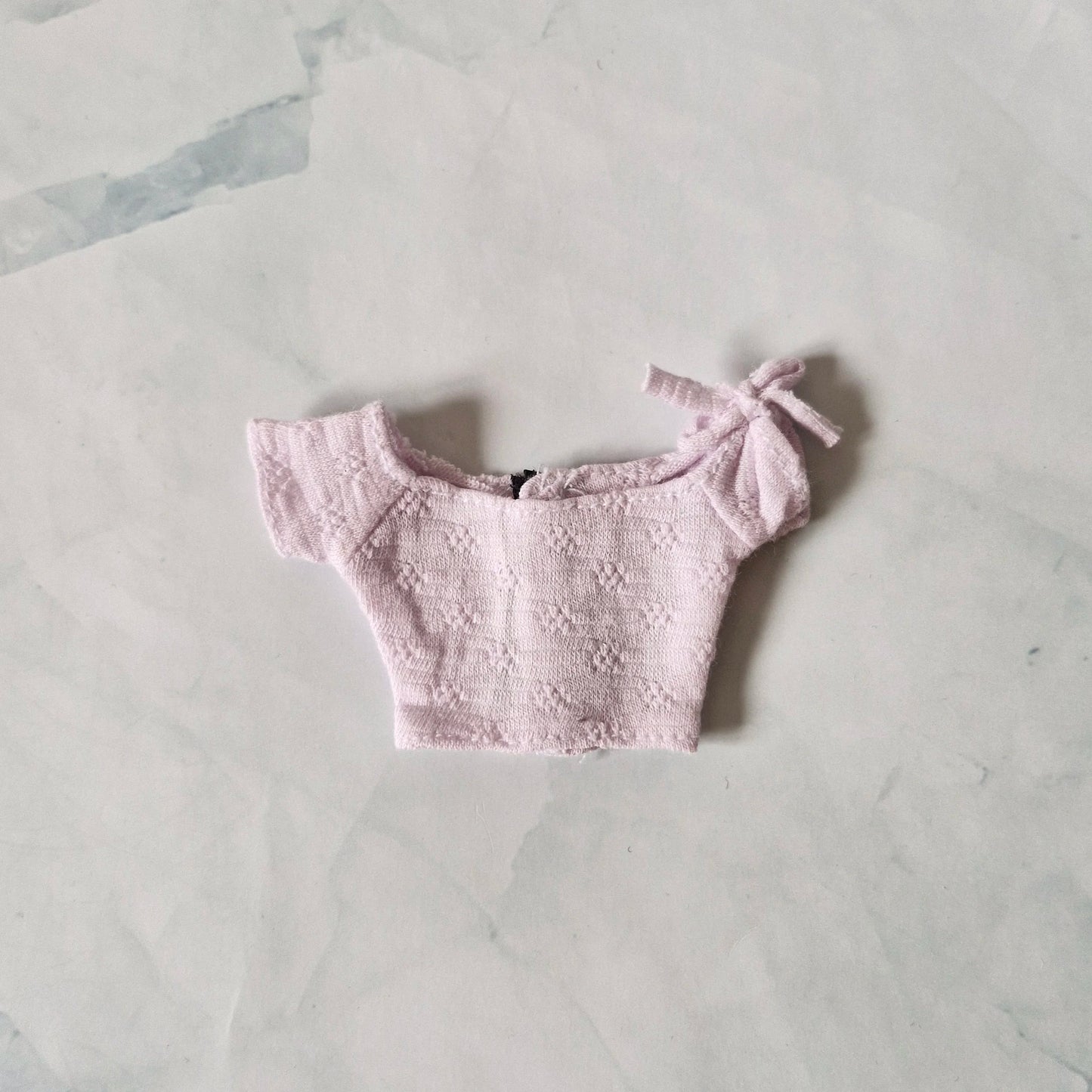 Pale lavender textured off-the-shoulder crop top for Barbie doll with tie detail on sleeve, laid flat.