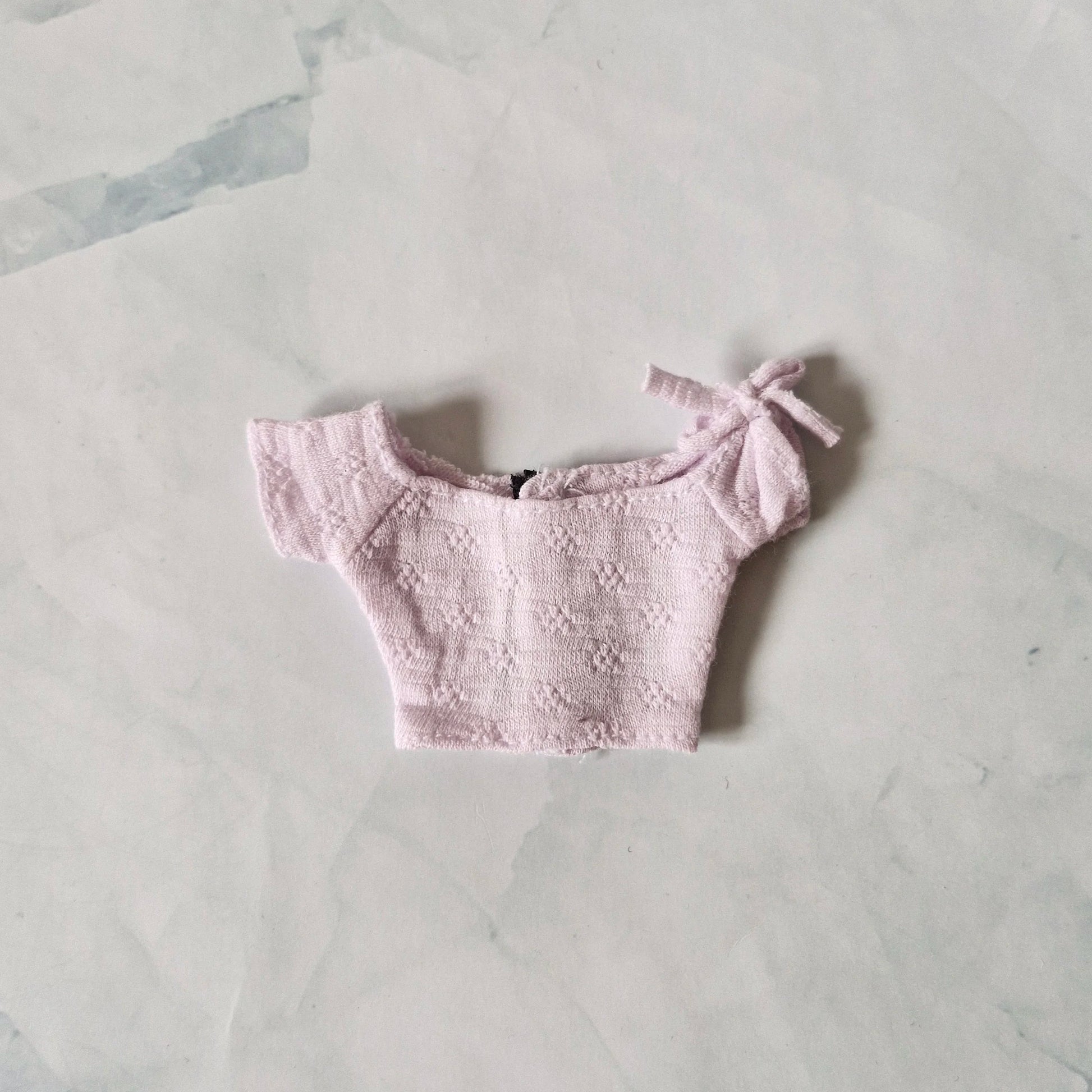Pale lavender textured off-the-shoulder crop top for Barbie doll with tie detail on sleeve, laid flat.
