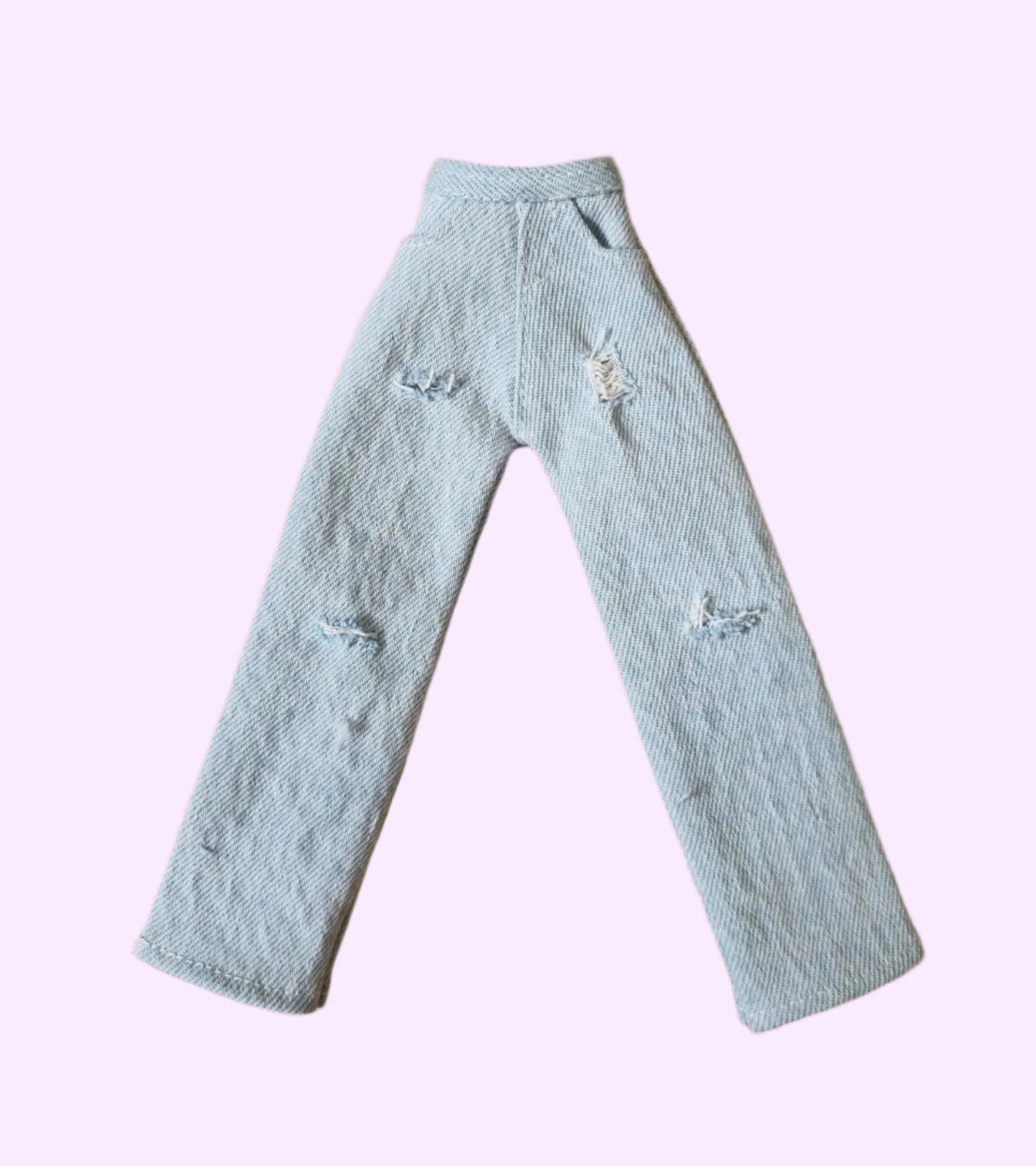 Handmade light blue distressed denim jeans for Barbie doll, laid flat on a brown textured background.