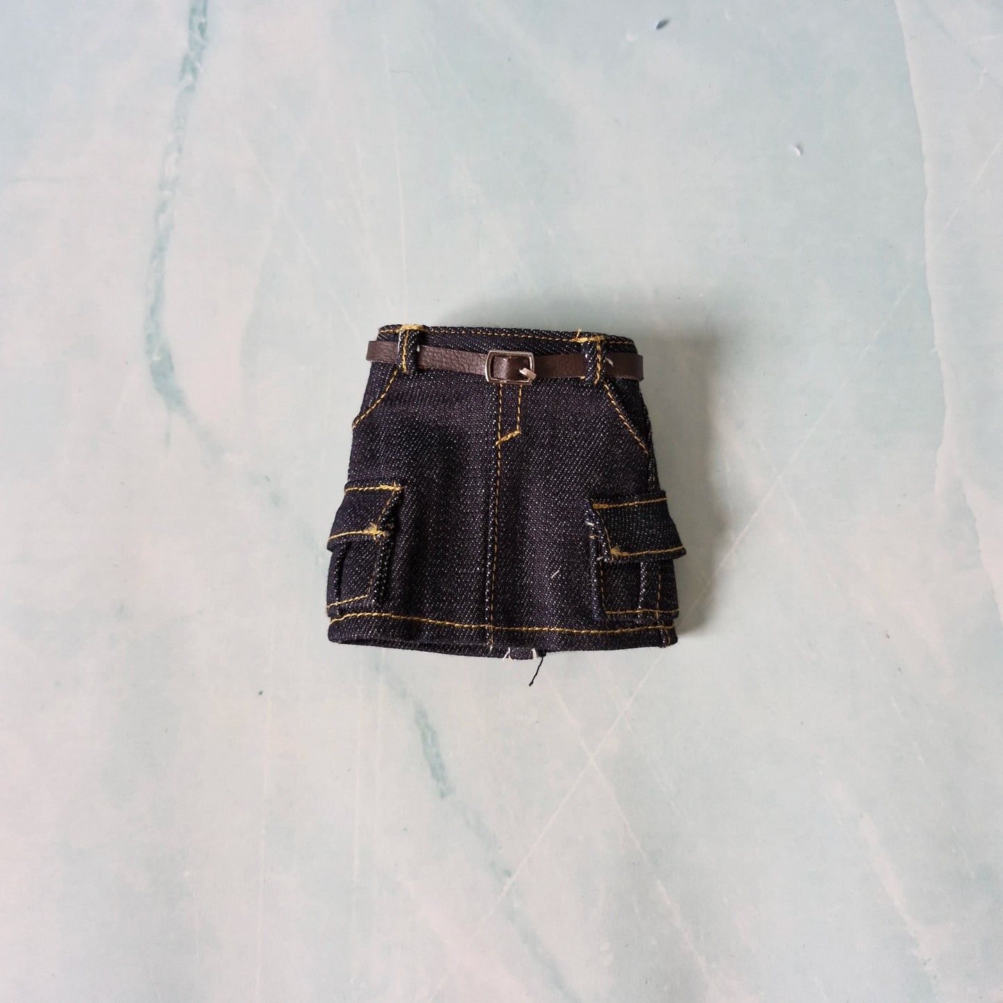 Black denim skirt with a belt on a light gray background