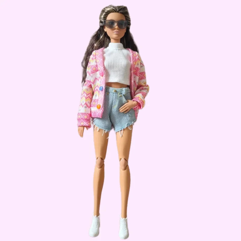 Barbie doll wearing a white cropped ribbed top, light blue denim shorts with frayed hems, a pink patterned cardigan with colorful buttons, white sneakers, and dark sunglasses..