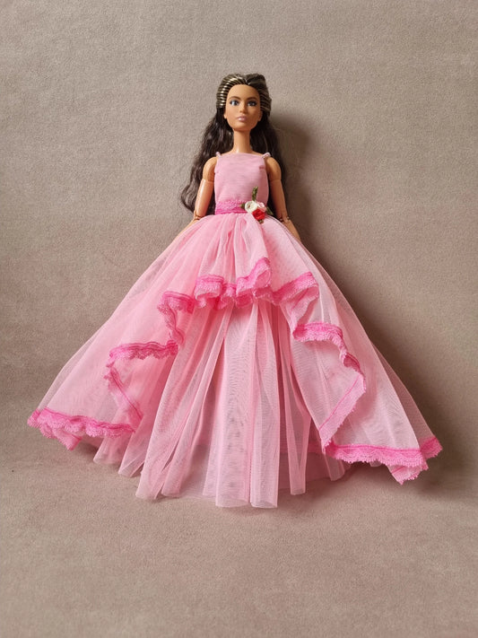 Brunette Barbie doll in full pink princess tulle ball gown with layered skirt and floral waist decoration against beige background.