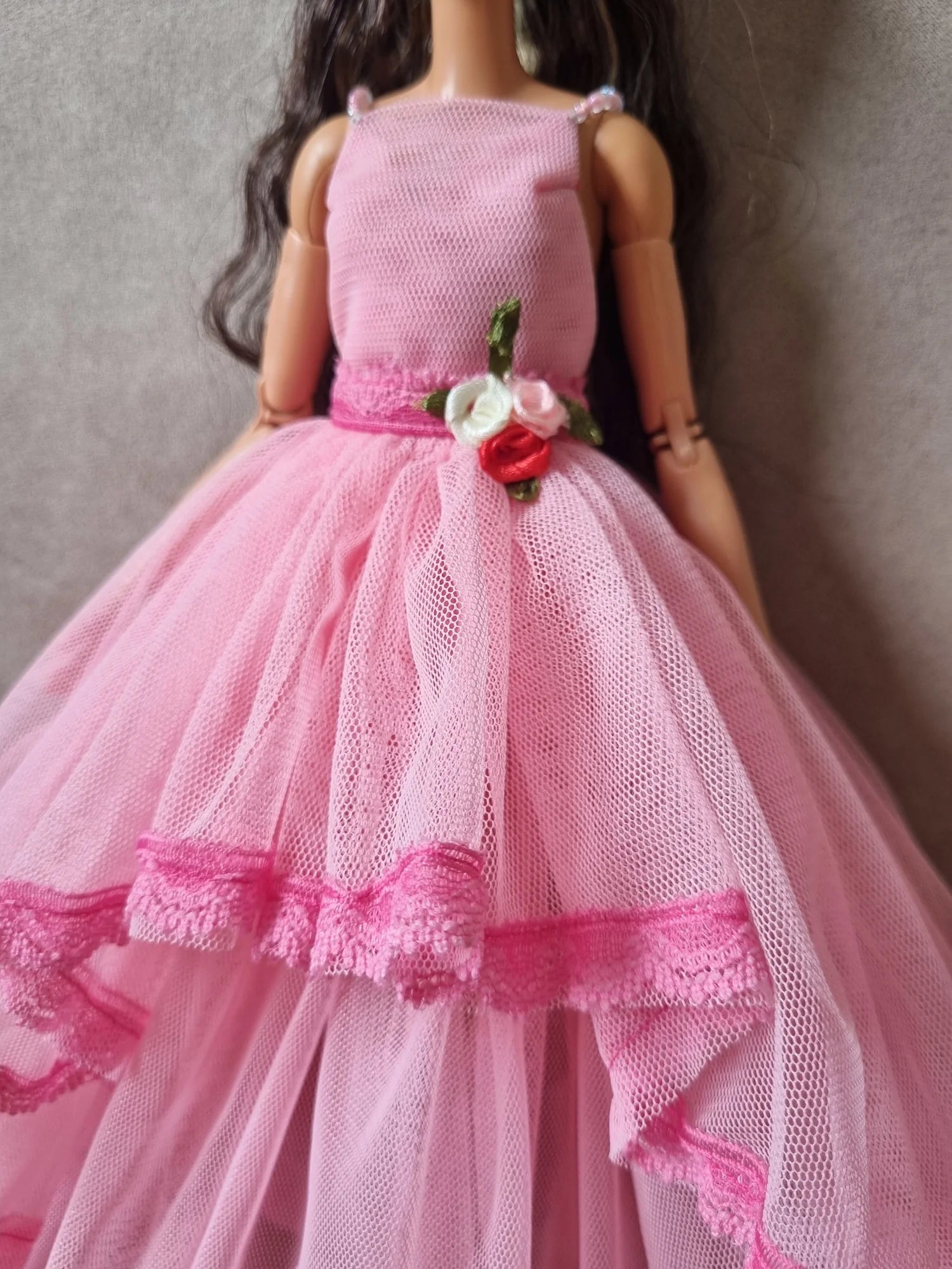 Close-up of Barbie doll wearing pink gown, showing sleeveless bodice, floral waist accent, and layered tulle skirt detail.
