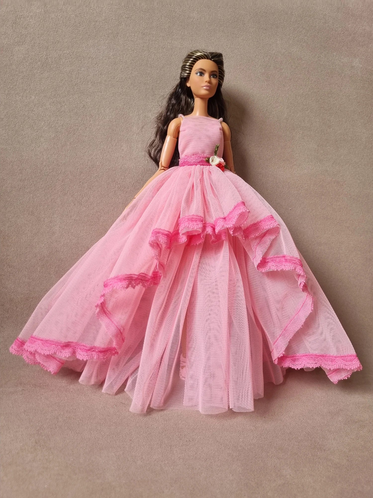 Elegant pink sleeveless ball gown with full tulle skirt, ruffles, and floral accent, worn by brunette Barbie doll.