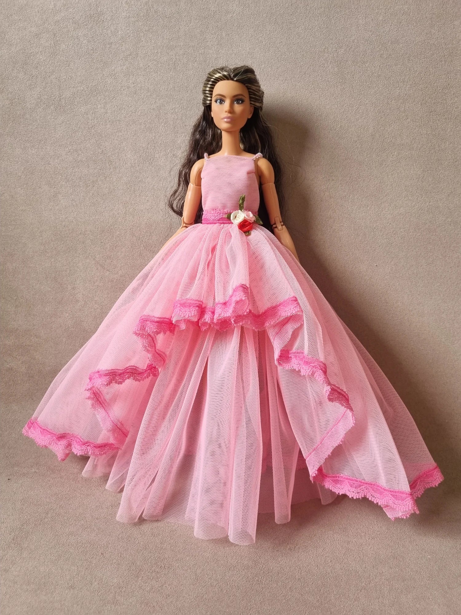 Fashion doll wearing romantic pink tulle gown with cascading ruffled layers and dark pink lace edging.