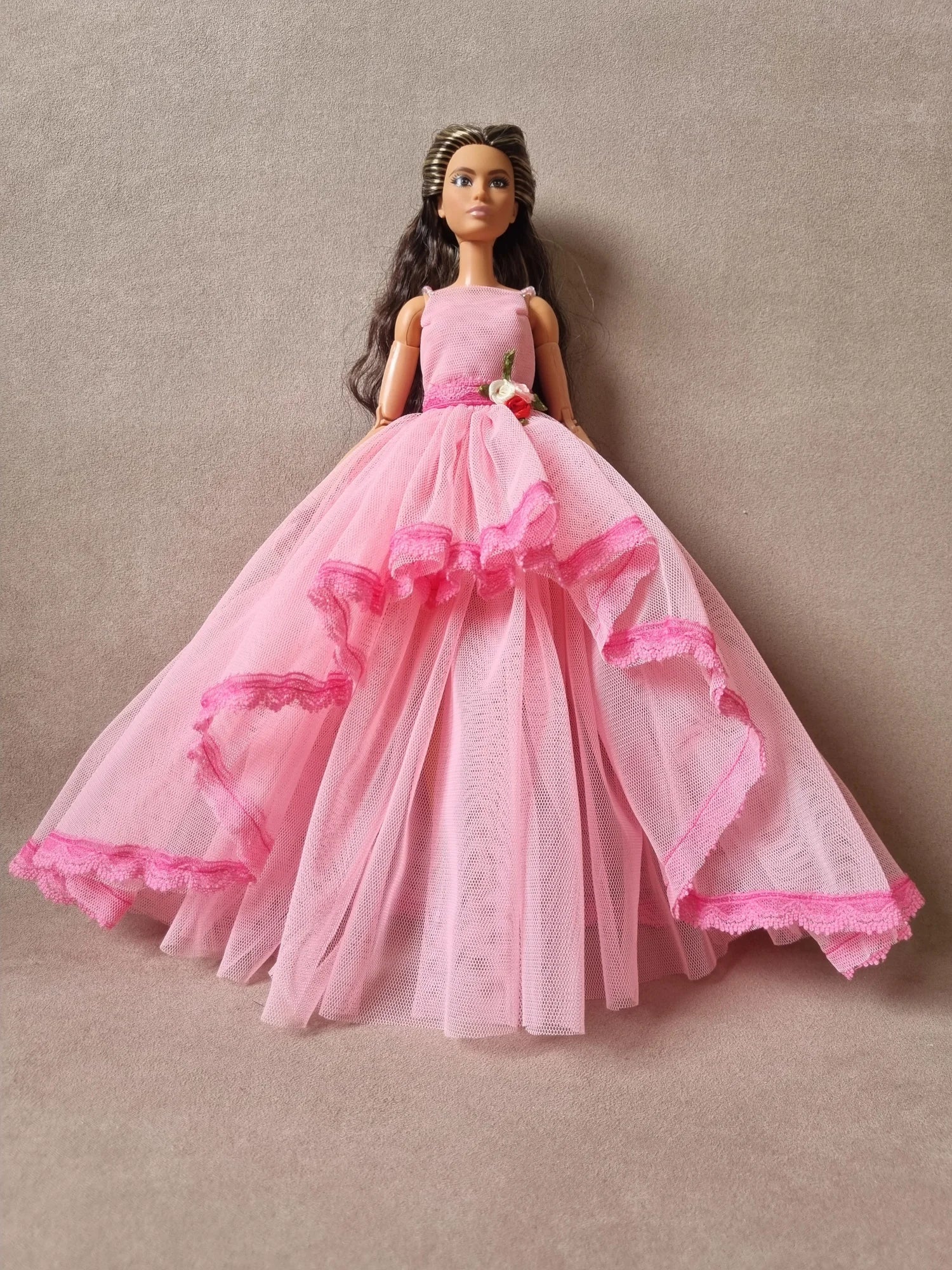 Brunette Barbie doll wearing elegant pink tulle ball gown with layered skirt, lace trim, and floral waist accent.
