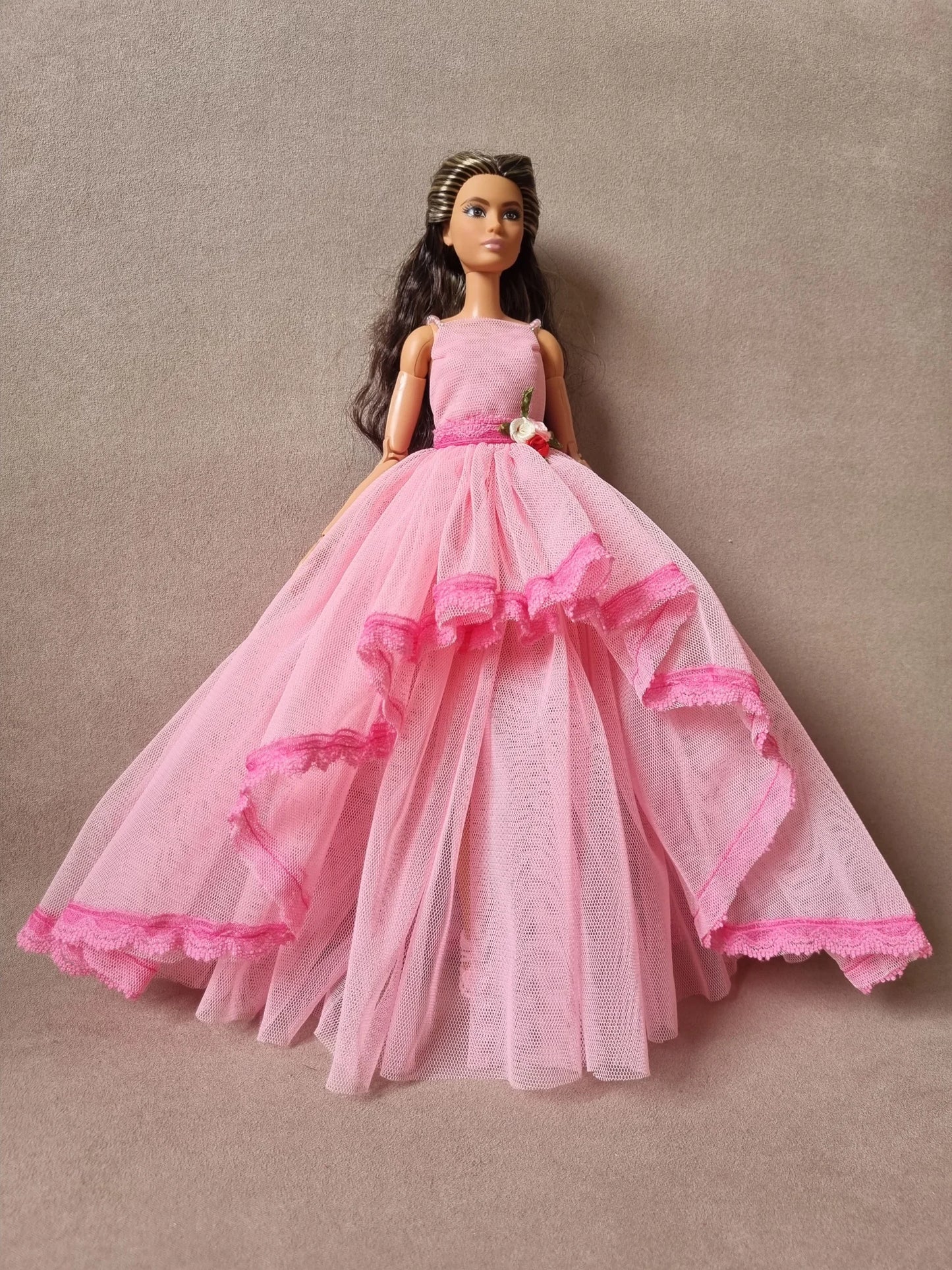 Barbie doll models stunning pink layered tulle ball gown, sleeveless with floral waist detail against beige background.
