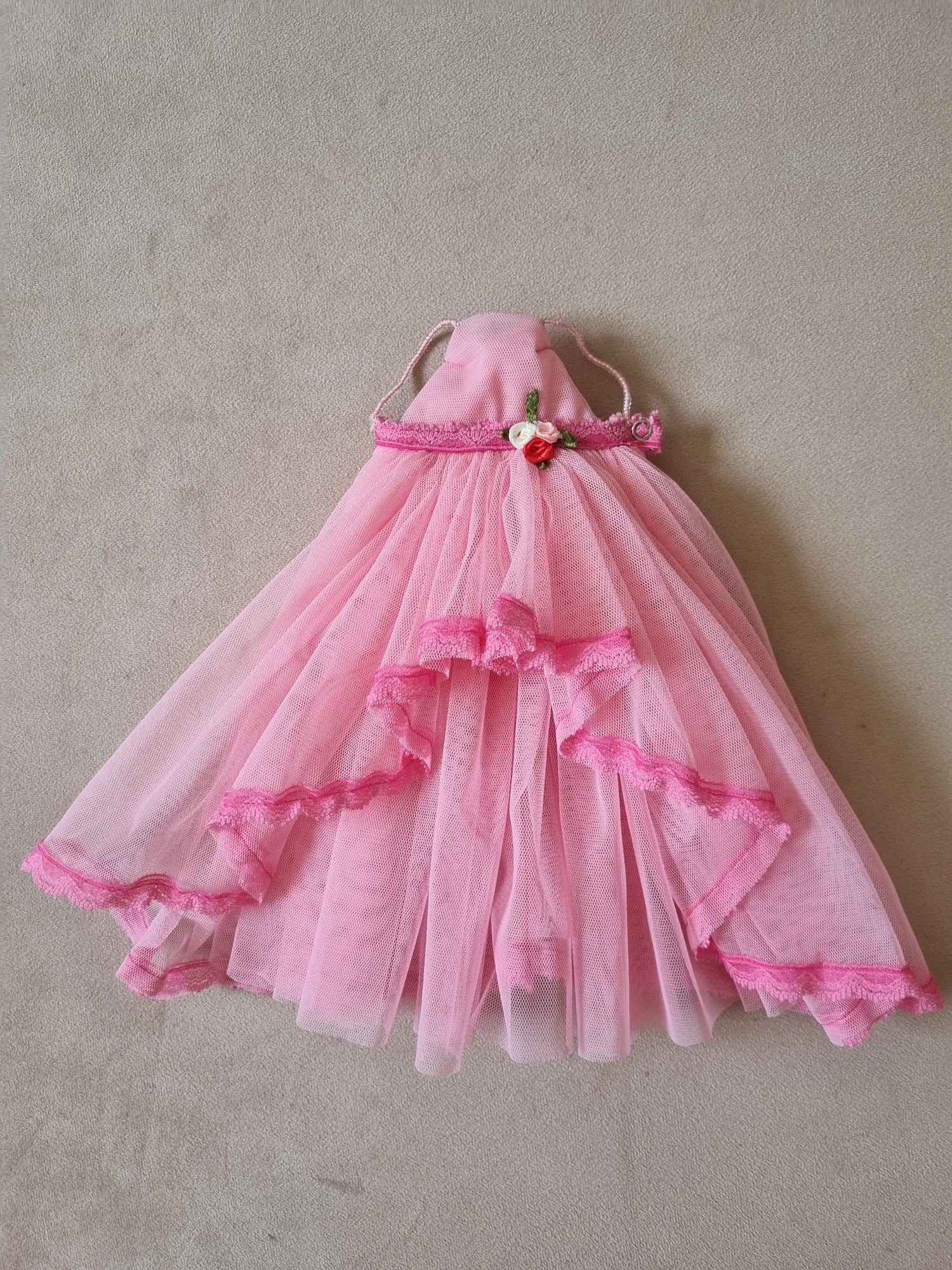 Pink tulle layered ball gown for Barbie doll with floral waist detail and lace trim, laid flat on beige background.