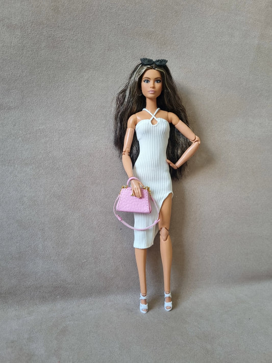 Brunette Barbie doll modeling white ribbed halter midi dress (sleeveless) with high slit, holding pink handbag, sunglasses on head.