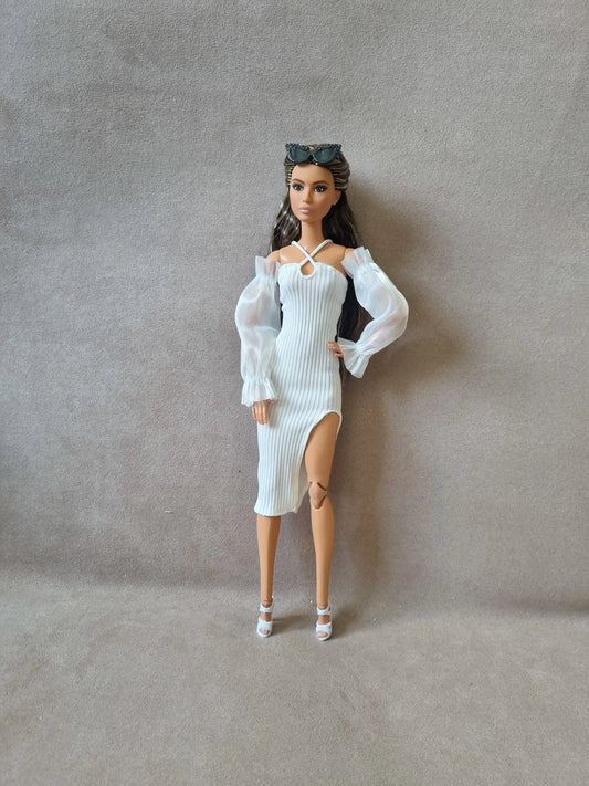 Brunette Barbie doll modeling white ribbed midi dress with crossover halter neck, high slit, and sheer puff sleeves, sunglasses on head.