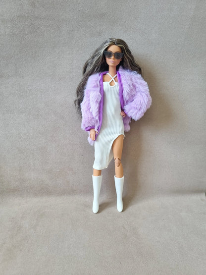 Barbie doll wearing white ribbed dress, lavender faux fur coat, sunglasses, and white knee-high boots against grey background.