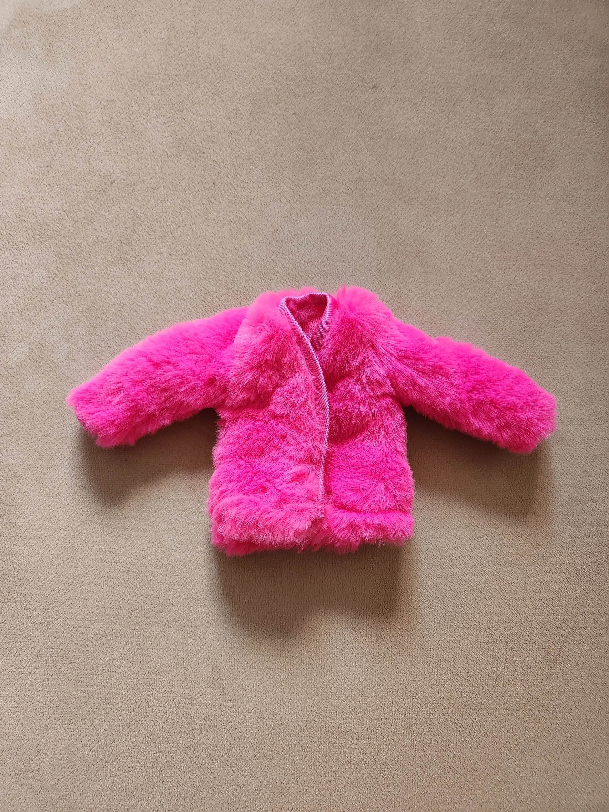 Hot pink faux fur open-front coat for Barbie doll, laid flat on beige background.