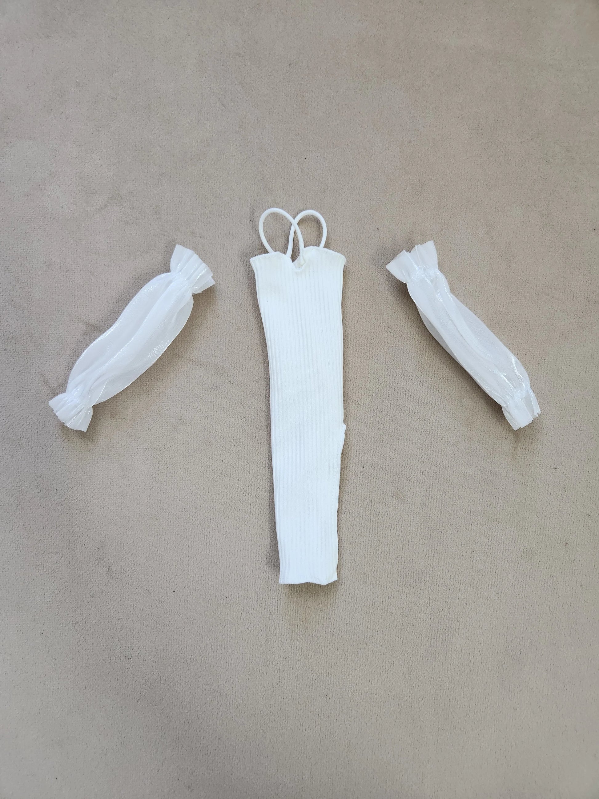 Barbie outfit components flat lay: white ribbed halter midi dress and separate sheer white puff sleeves on beige background.