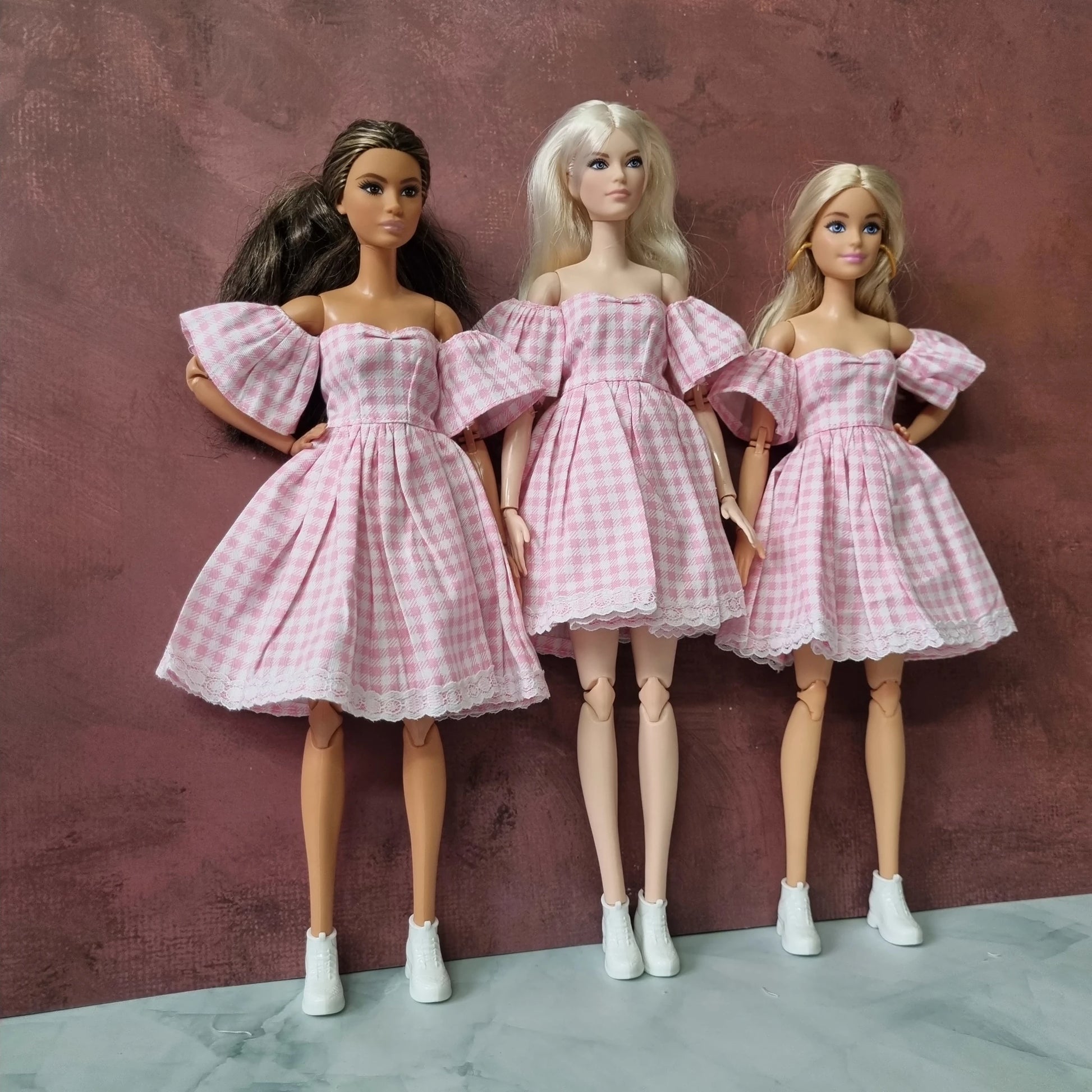 Three Barbie dolls in matching pink checkered dresses with puff sleeves